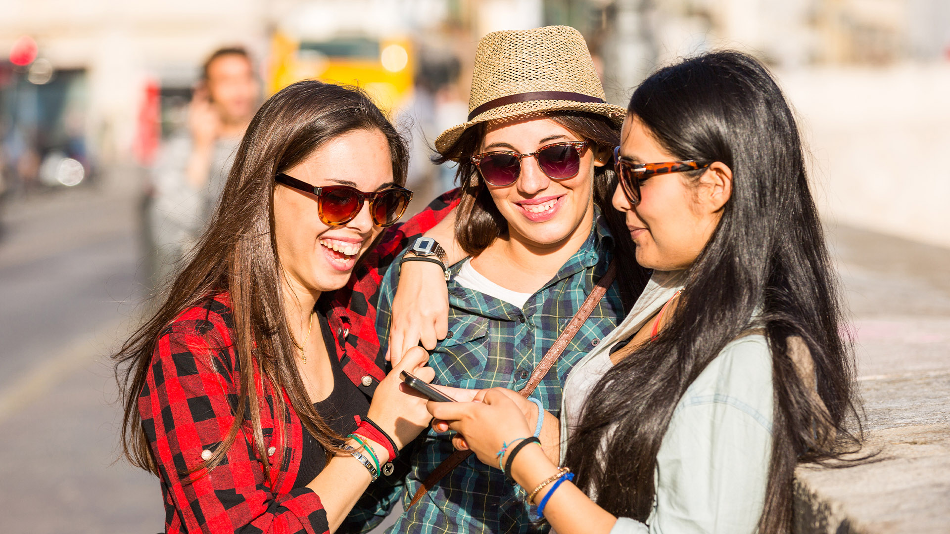 Group of three women laughing while looking at smartphone