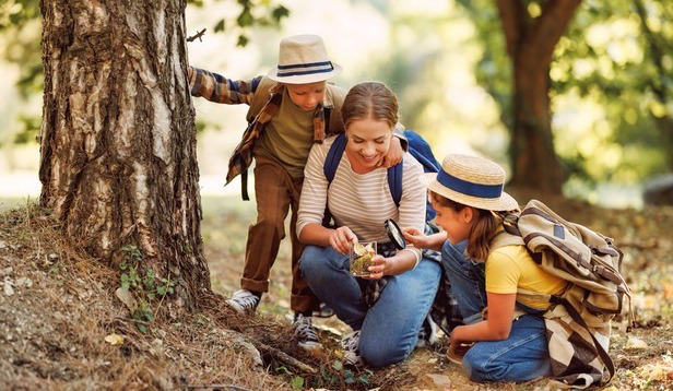 Family examining forest environment with magnifying glass.