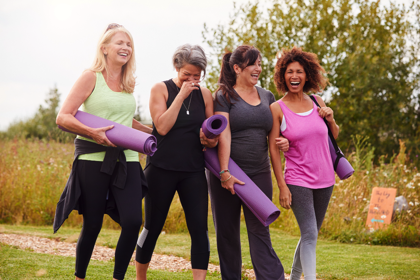 Four women smiling while walking and holding yoga
mats